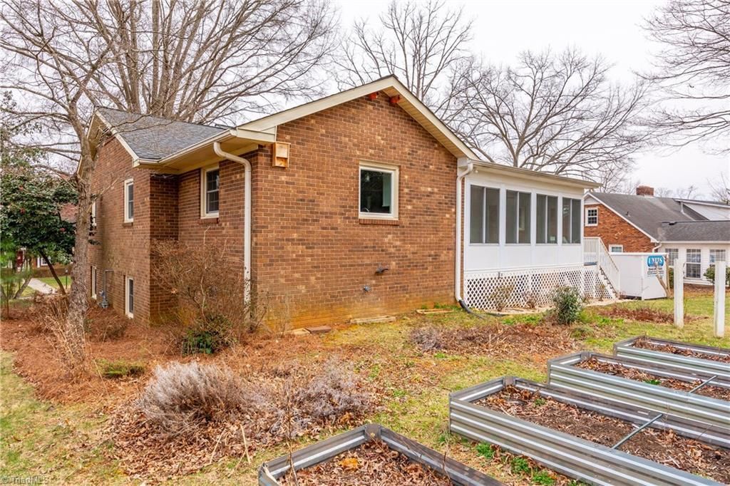 Brick house with a screened porch, leaf-covered yard, and raised garden beds in the foreground