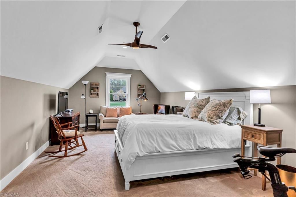 Bright attic bedroom with a large bed, sitting area, and sloped white ceiling.