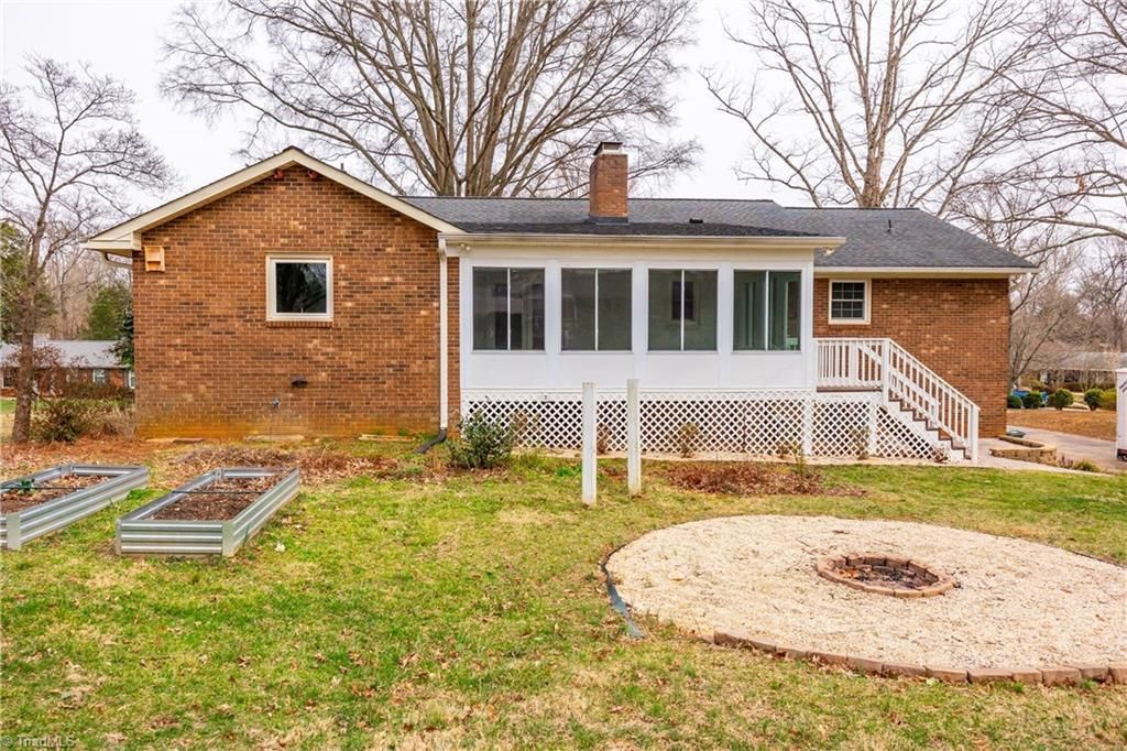 Rustic house with wood siding, screened porch, flower beds, and a circular gravel fire pit in the yard