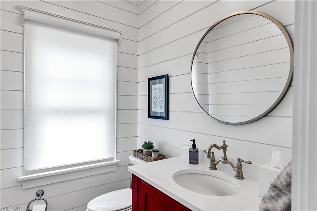 Bright white bathroom with round mirror, window, and red vanity beneath striped wall paneling
