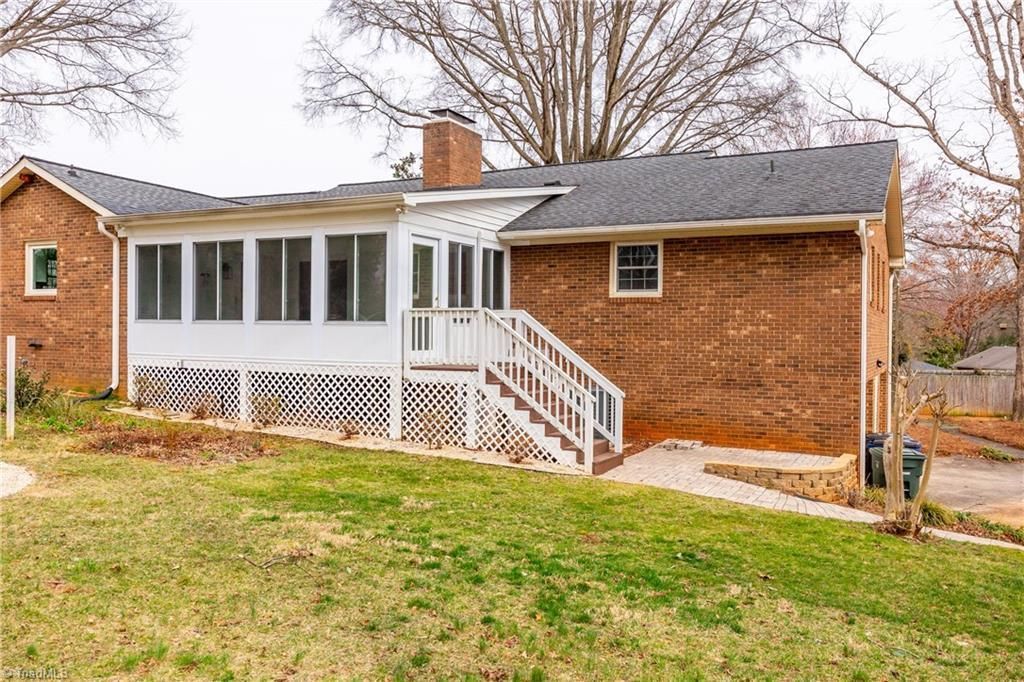 Brick house with white porch and stairs on a grassy yard in a leafless suburban setting