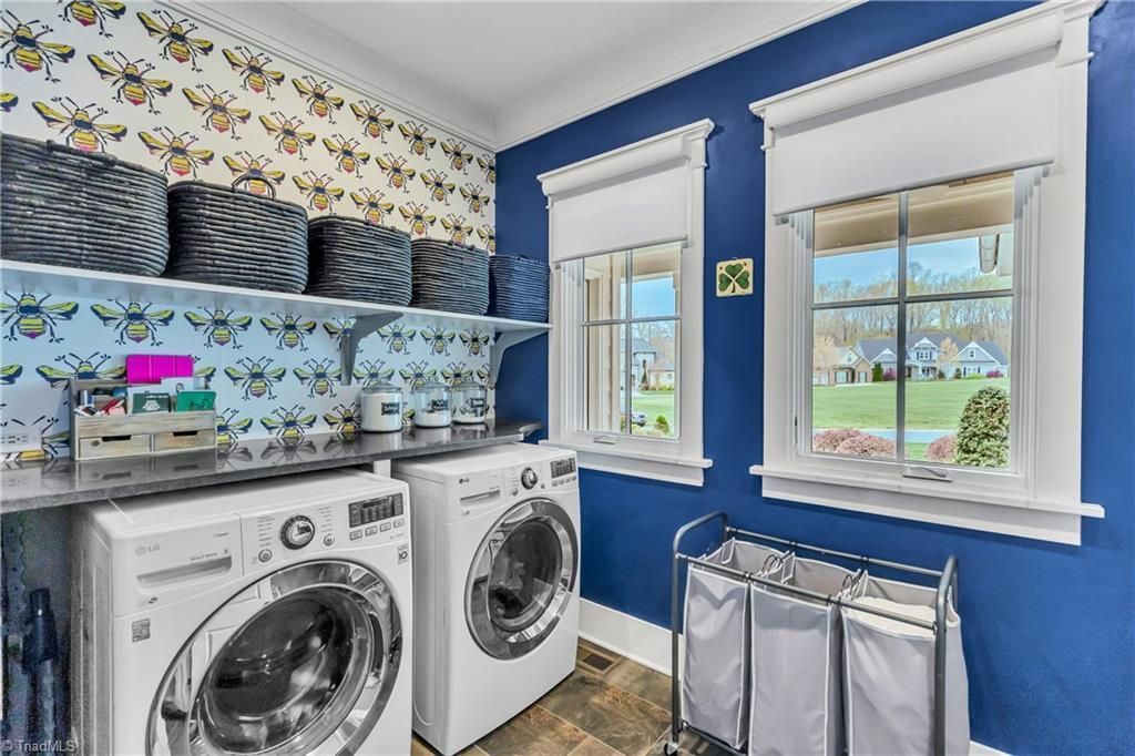 Bright laundry room with white washer and dryer, blue walls, floral wallpaper, and two windows