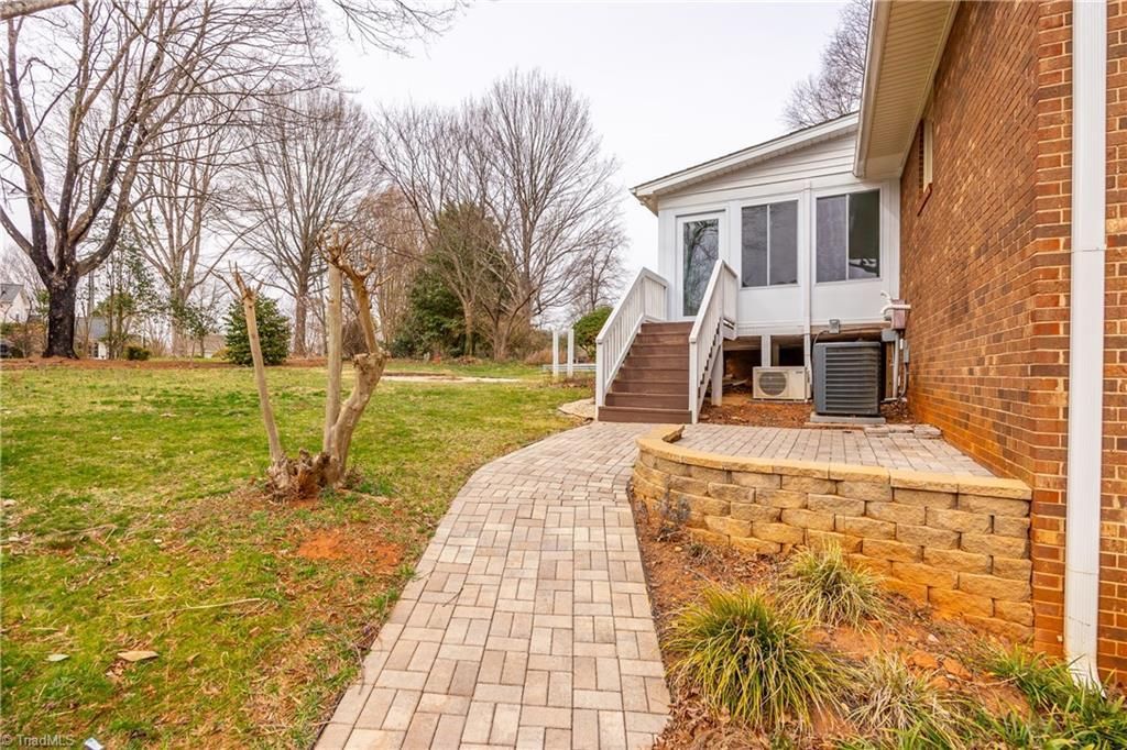 Brick walkway beside a brick house leading to a white porch, with grassy yard and bare trees in fall.