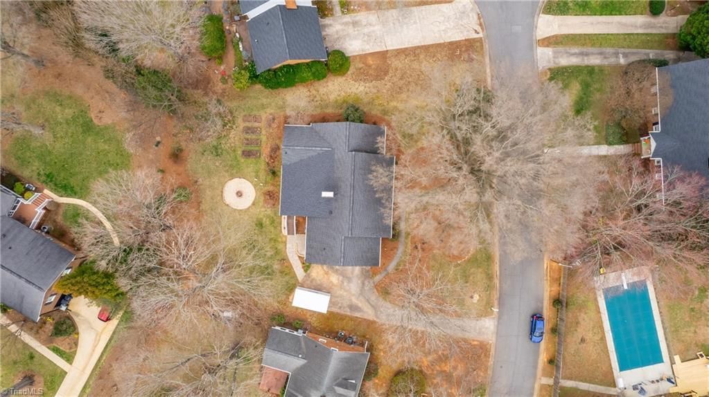 Aerial view of a residential yard with houses, trees, a driveway, and a blue swimming pool