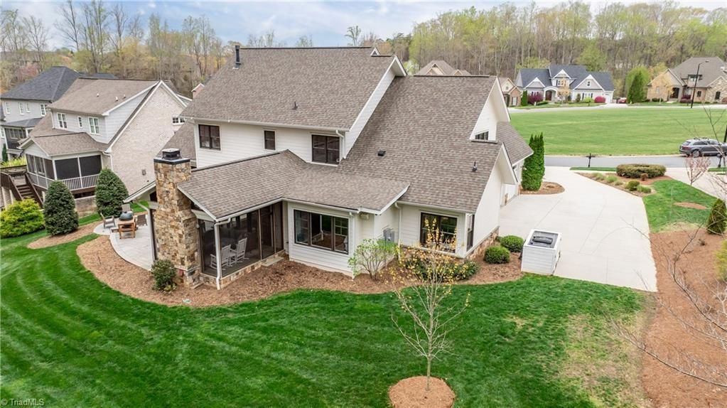Aerial view of a suburban house with a large green lawn, driveway, and neighboring homes.