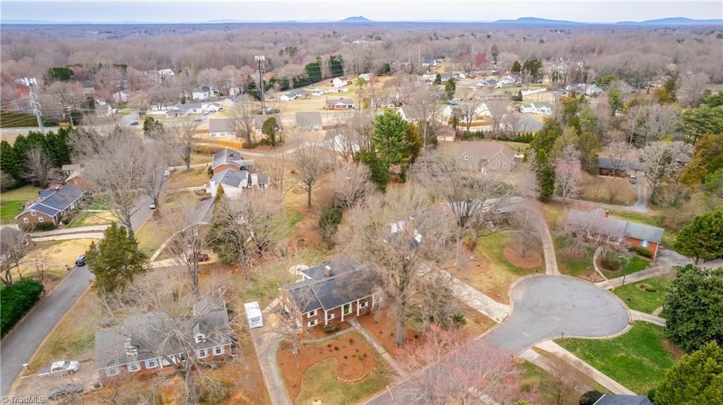 Aerial view of a suburban neighborhood with houses, trees, roads, and a distant horizon.