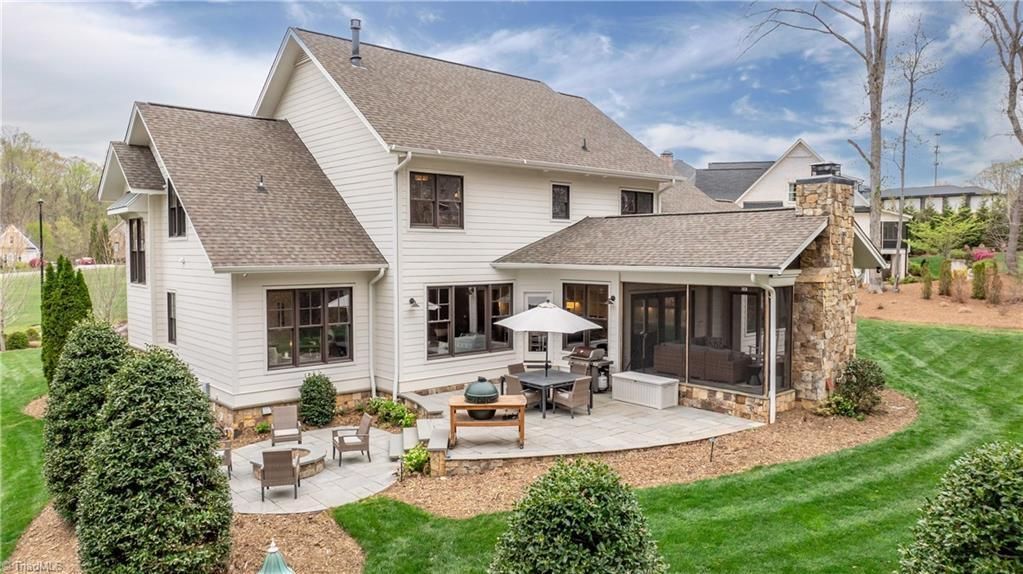White two-story house with a patio, outdoor seating, and a landscaped yard under a cloudy sky