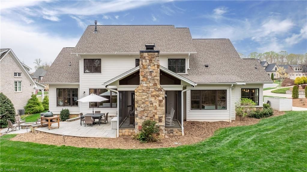 Backyard view of a suburban house with a stone chimney, patio seating, and a green lawn