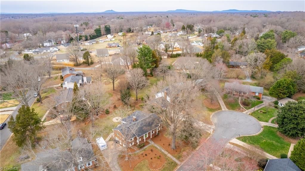Aerial view of a wooded suburban neighborhood with scattered houses and curving roads.