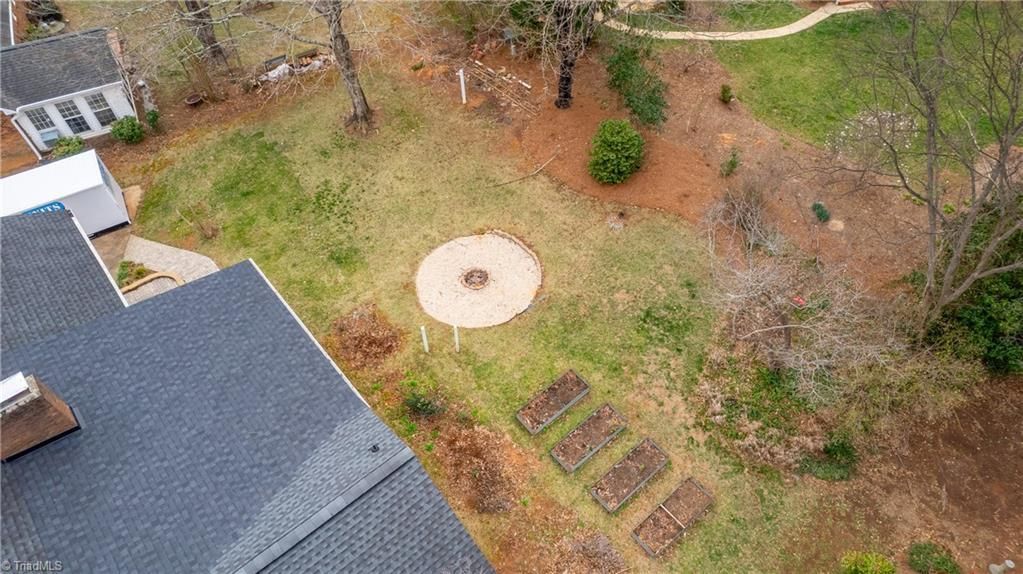 Aerial view of a backyard with a circular patio, garden beds, and a house roof on the left.