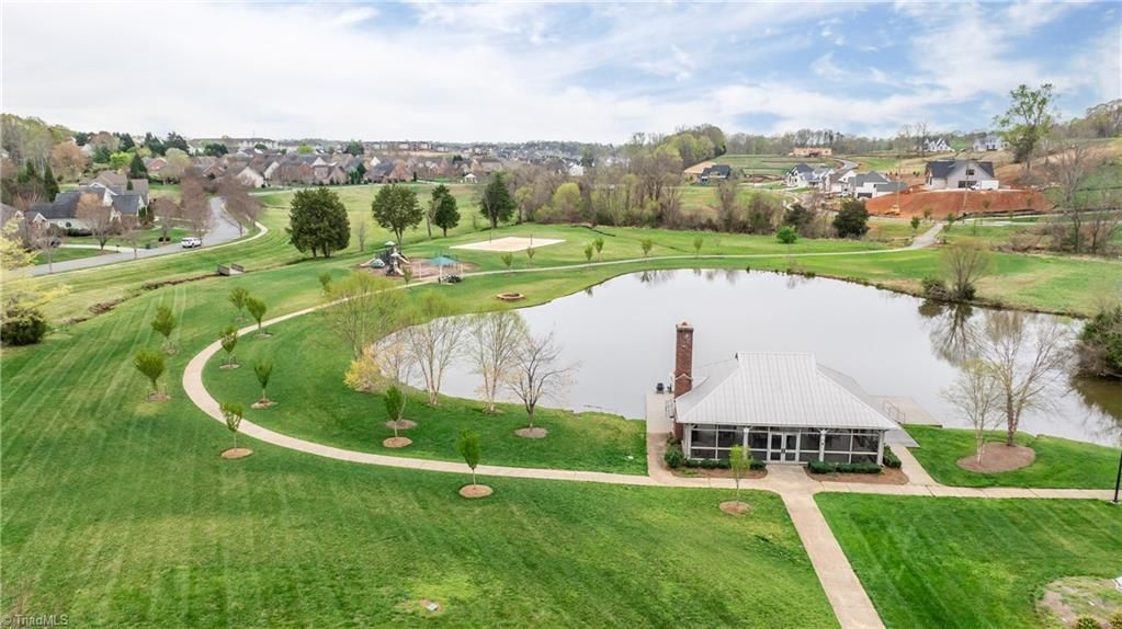 Aerial view of a green park with walking paths, a pond, and a small pavilion under a cloudy sky