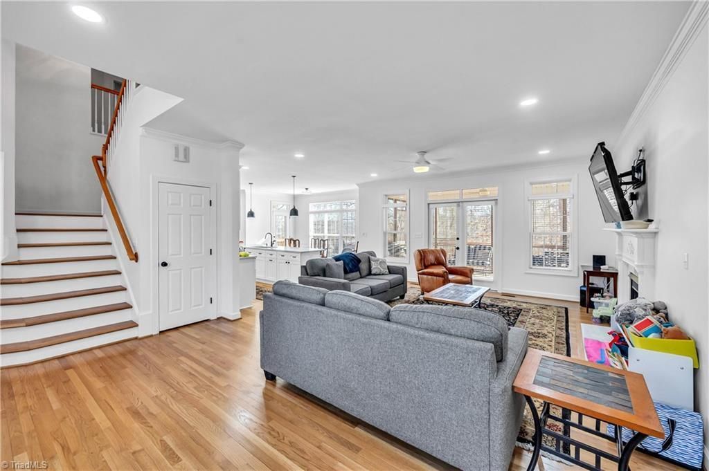 Bright open living room with gray sofas, hardwood floors, staircase, and white walls