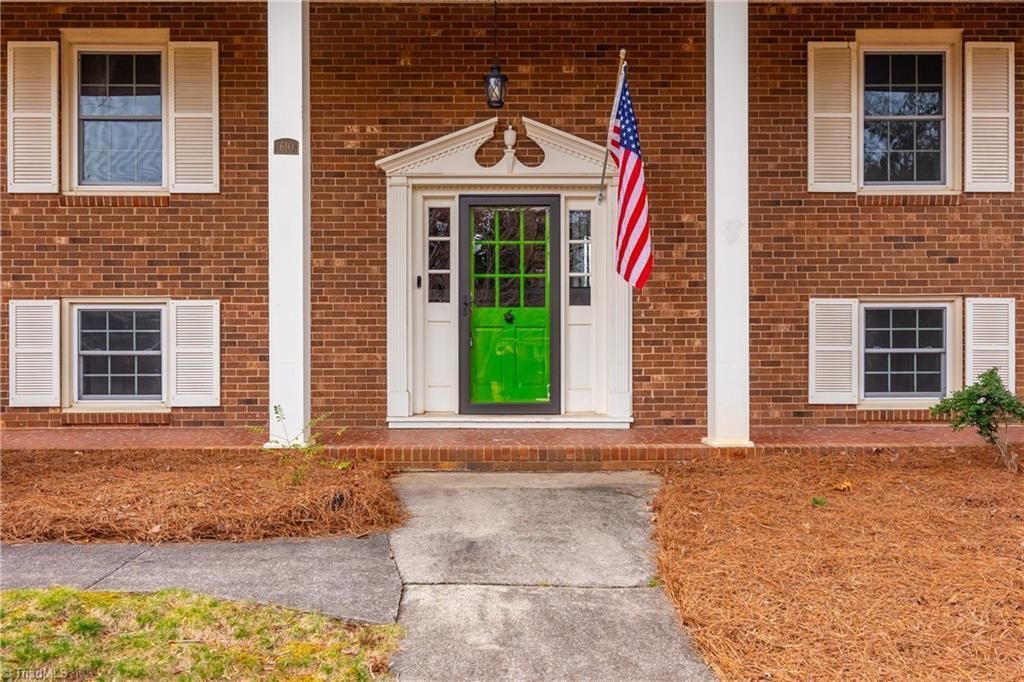 Brick apartment entrance with green door, American flag, and white-trimmed windows amid fallen leaves