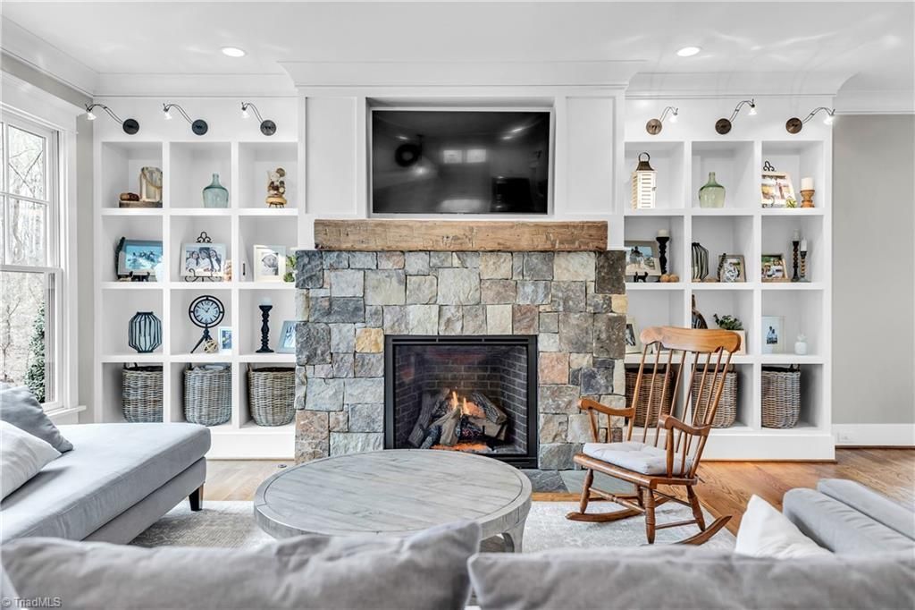 Bright living room with stone fireplace, built-in shelves, TV, and gray seating