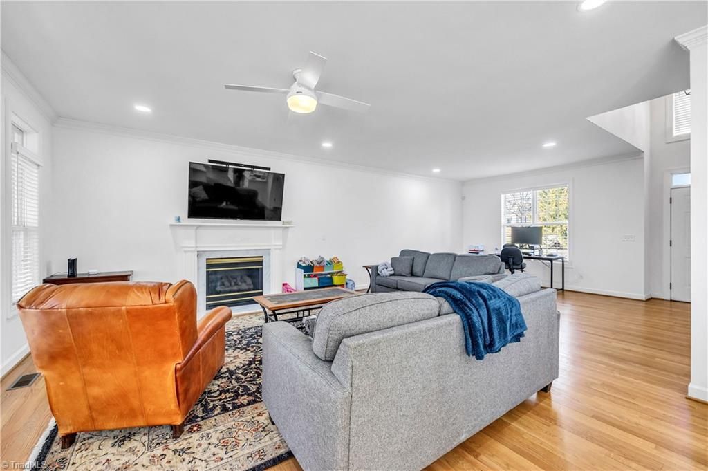 Bright living room with gray sofa, orange chair, fireplace, TV, and hardwood floors