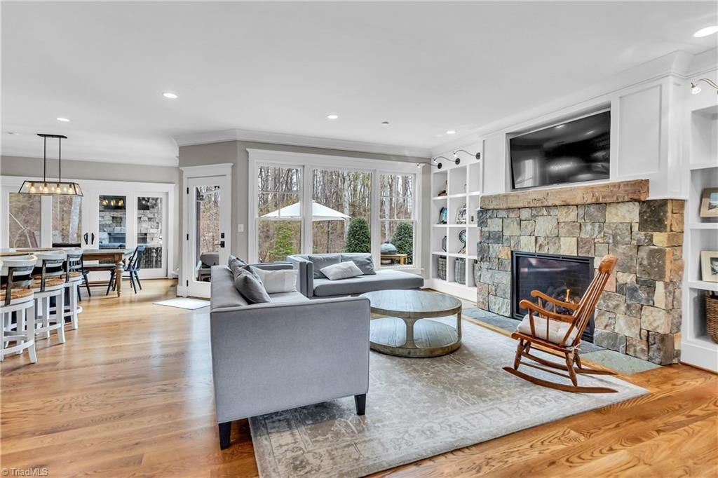 Bright living room with gray sofa, rocking chair, stone fireplace, and large windows over hardwood floors