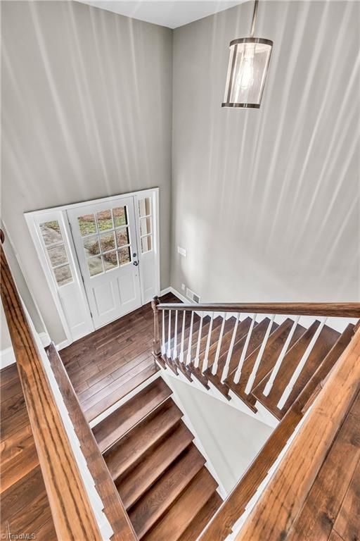 Wooden staircase with white walls and a hanging light fixture, viewed from the landing.