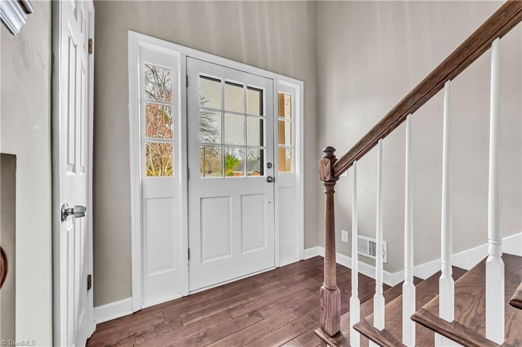 Bright foyer with white double doors, wood floor, and staircase railing on the right