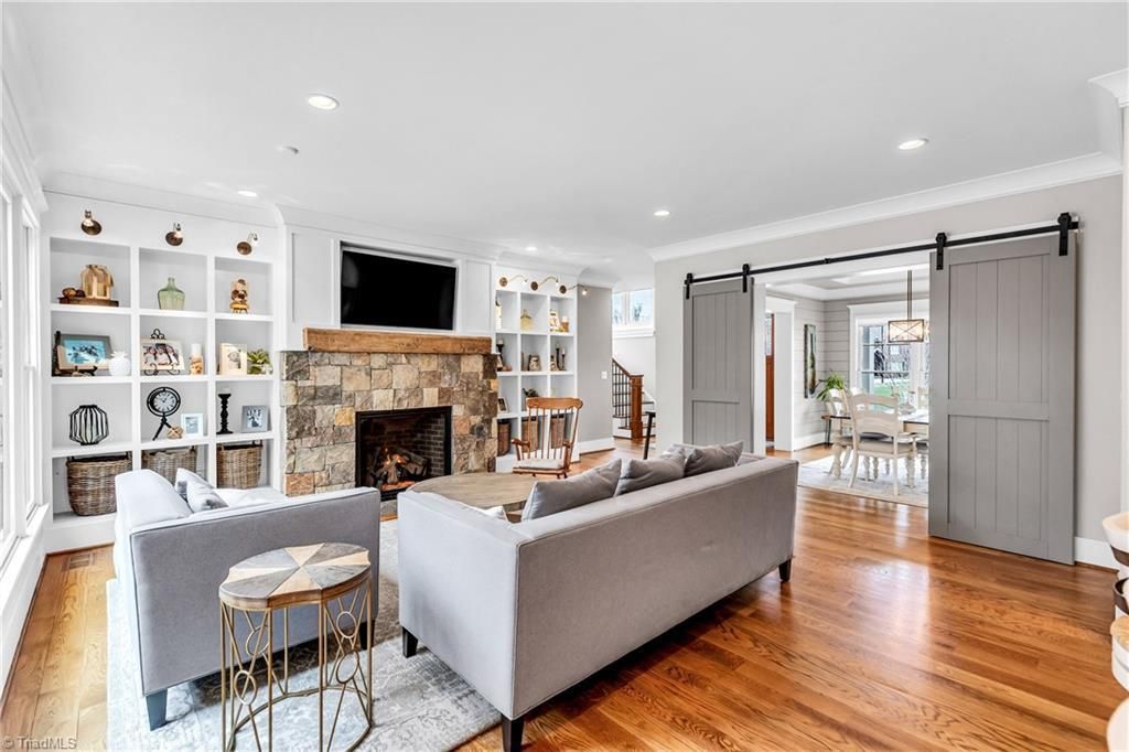 Bright living room with gray sofas, stone fireplace, white shelving, and hardwood floors