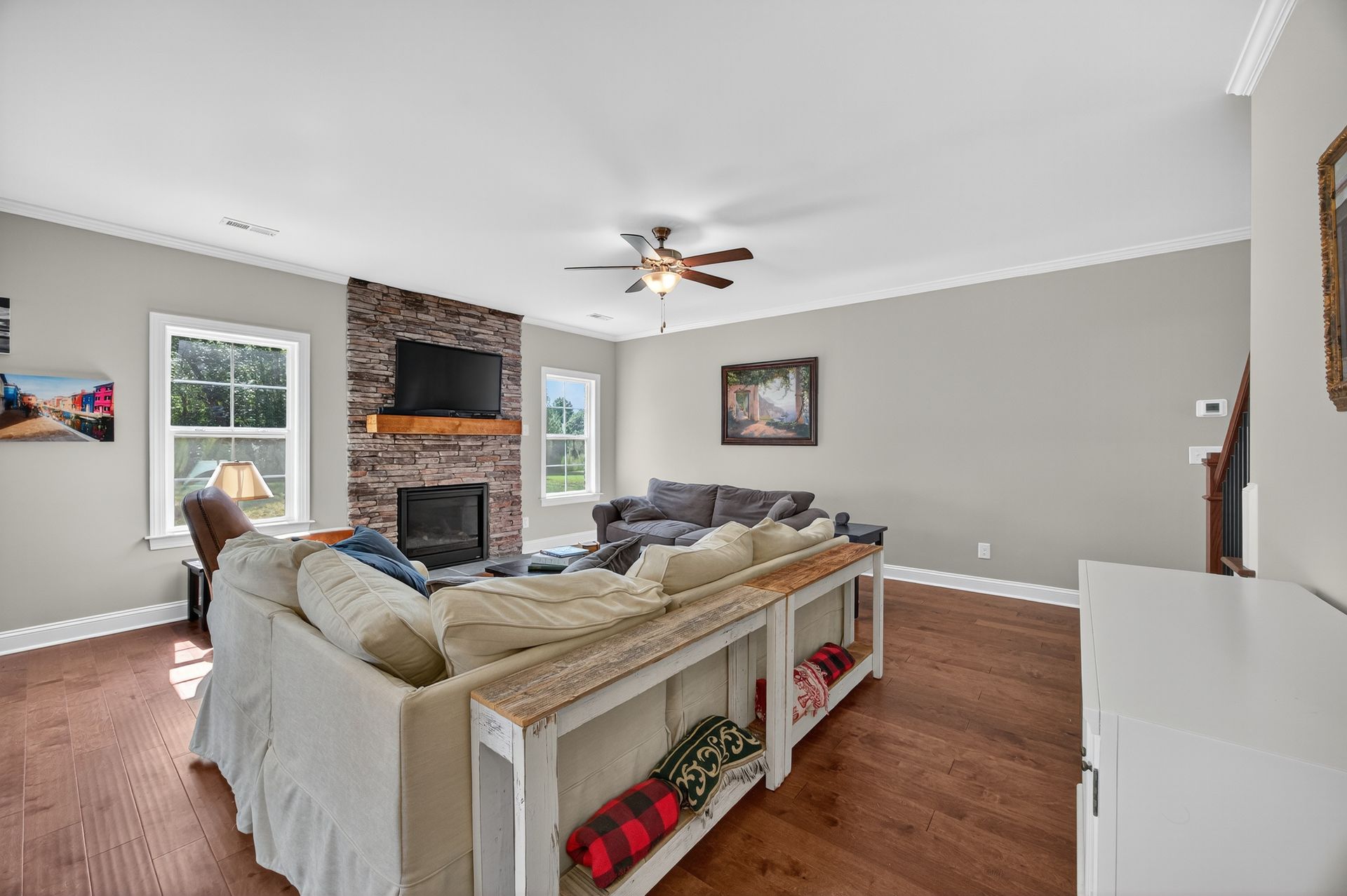 Bright living room with beige sectional, stone fireplace, wall-mounted TV, and wood floors