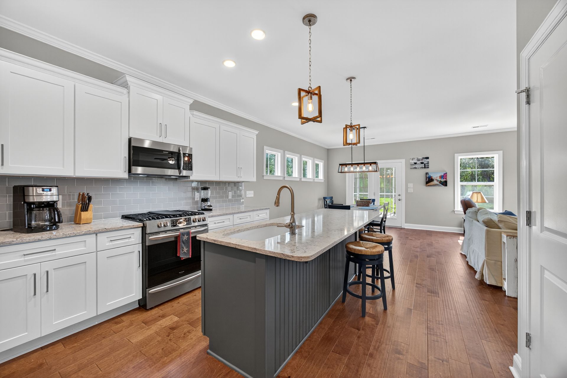 Bright modern kitchen with white cabinets, gray island, stainless appliances, and hardwood floors