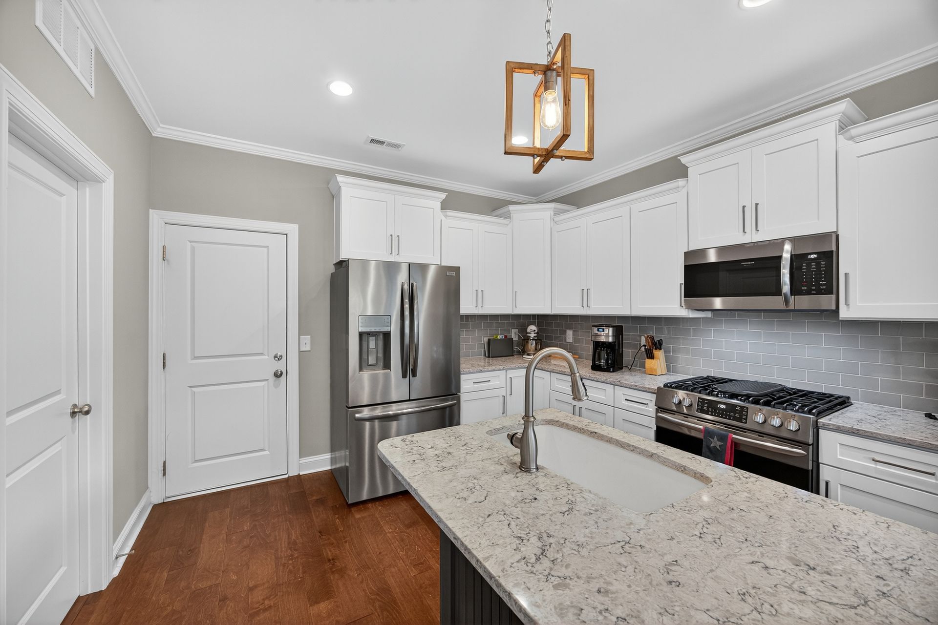 Modern white kitchen with granite island, stainless steel appliances, and hardwood floors