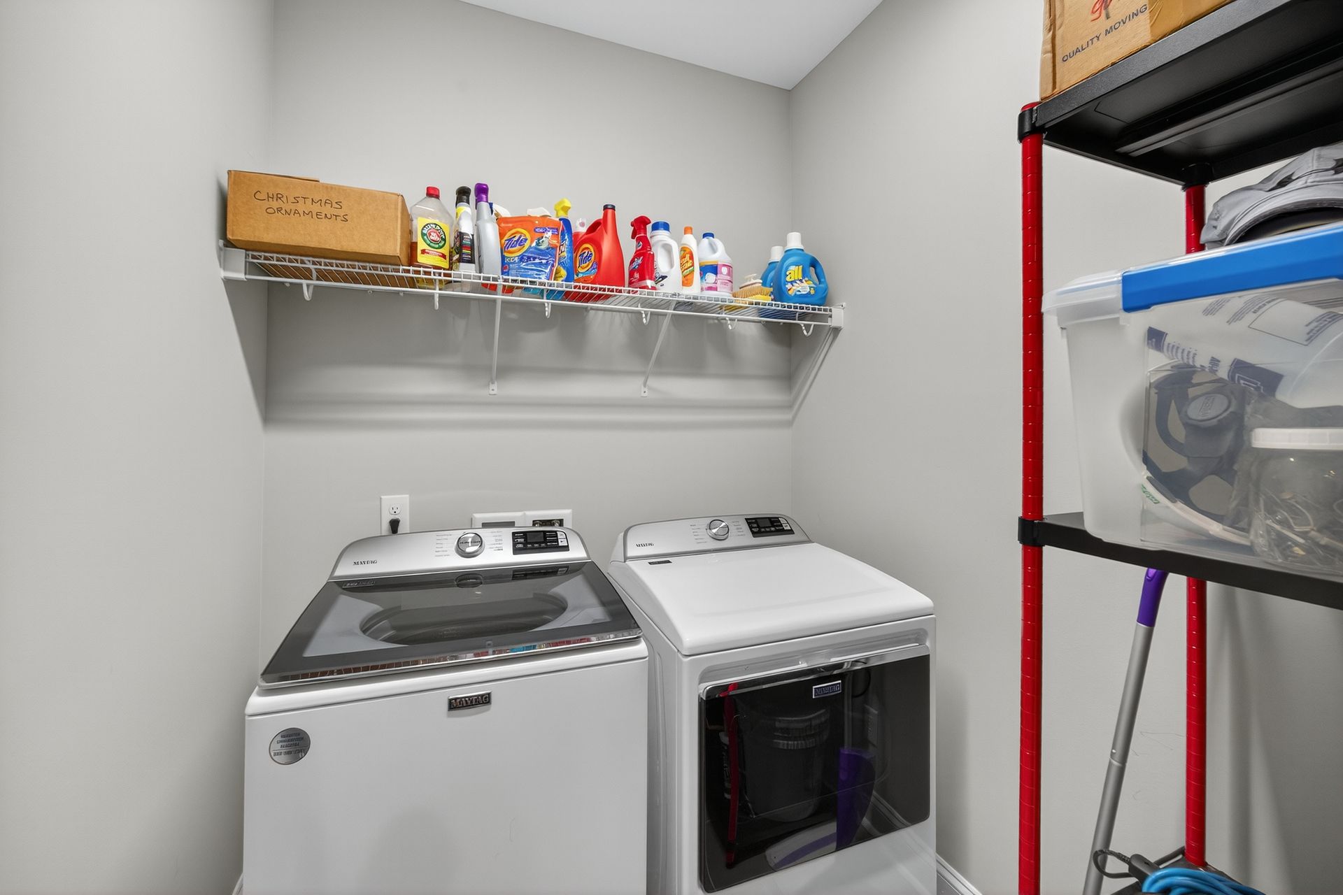Laundry room with white washer and dryer, shelf of detergents, and storage rack.