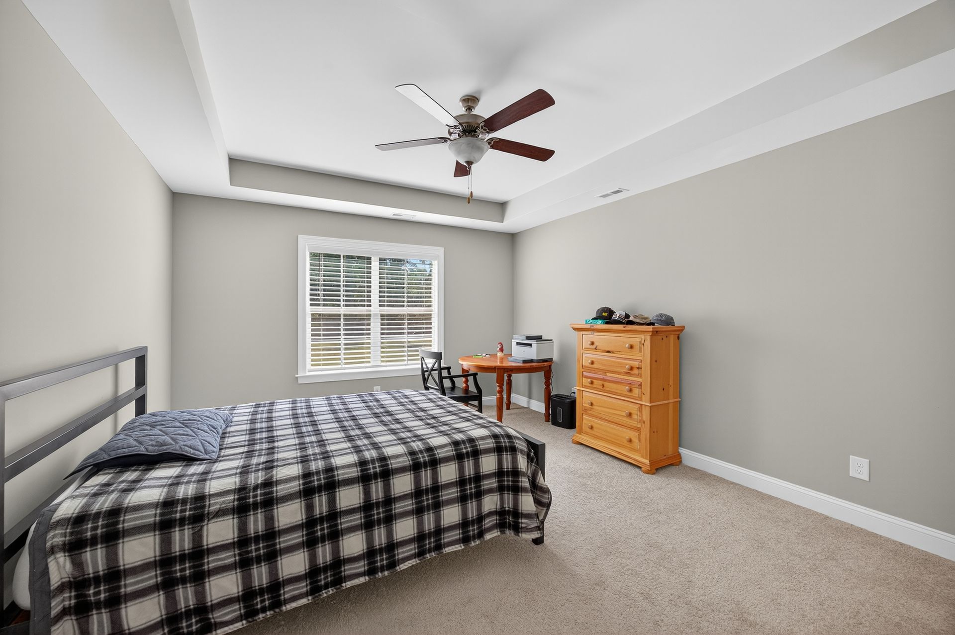 Neat bedroom with a bed, dresser, desk, and ceiling fan under a sloped ceiling.