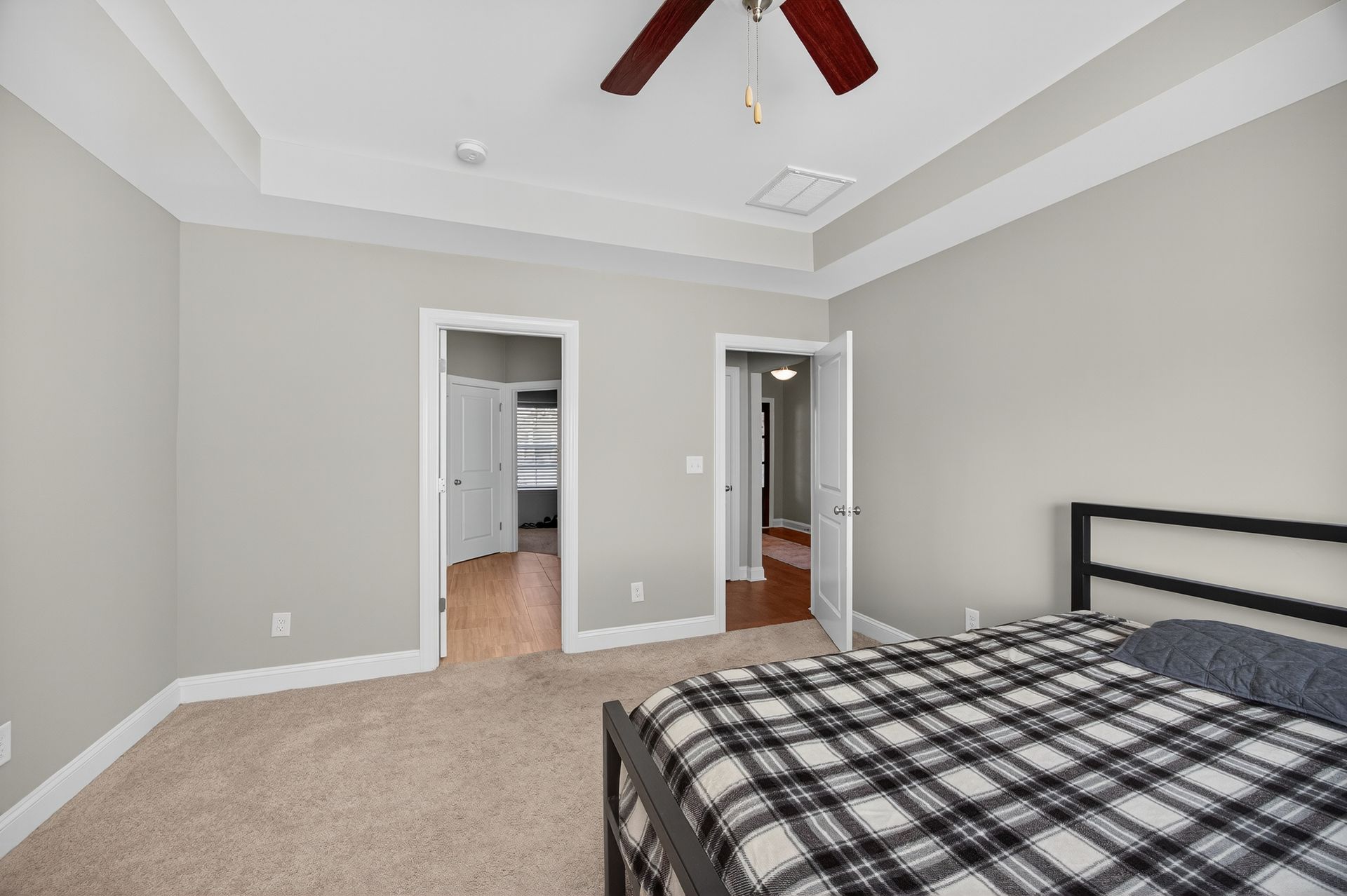 Empty bedroom with gray walls, beige carpet, ceiling fan, and open doors to a hallway and closet.