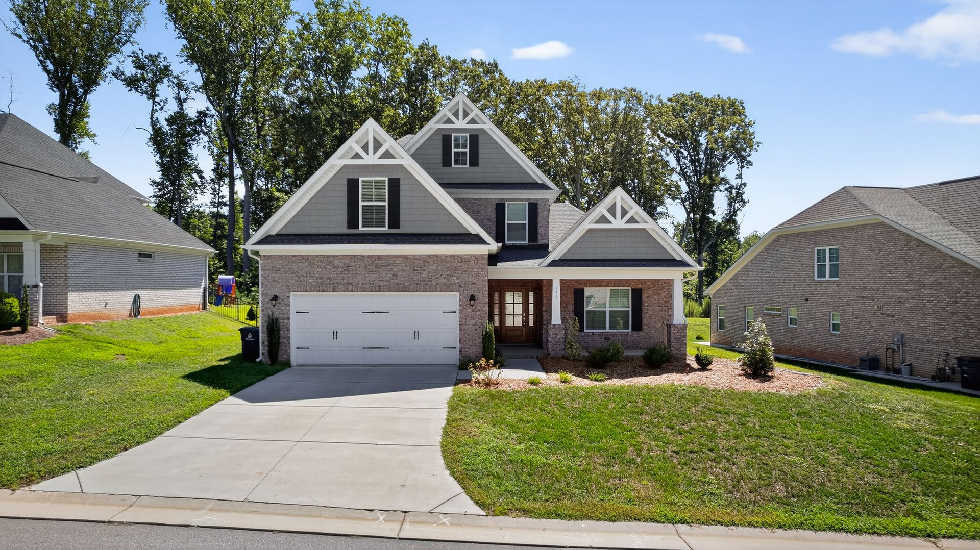 Suburban two-story gray house with white garage, front porch, and driveway on a sunny day