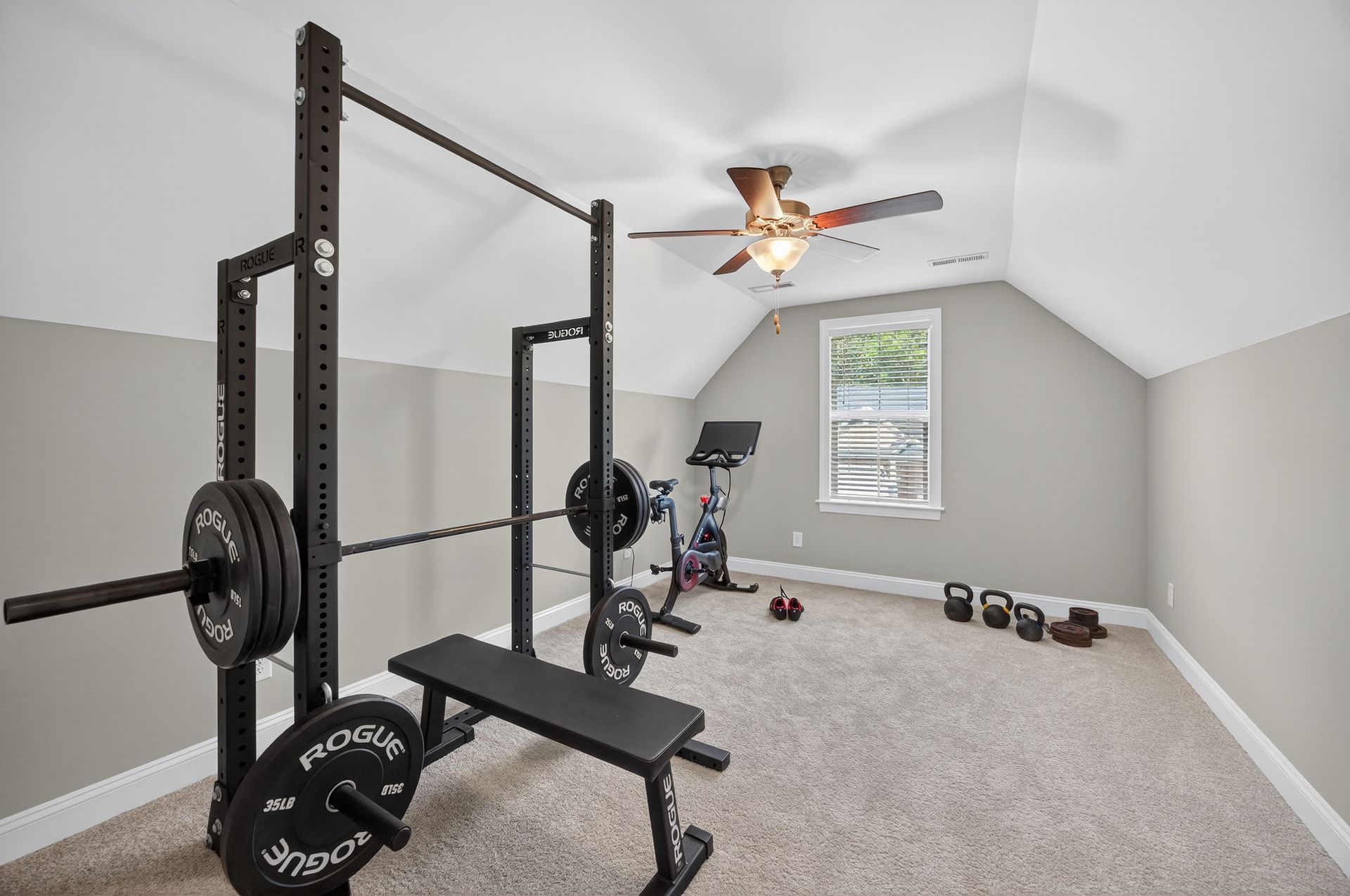 Home gym with squat rack, bench, weights, exercise bike, dumbbells, and a ceiling fan in a carpeted room