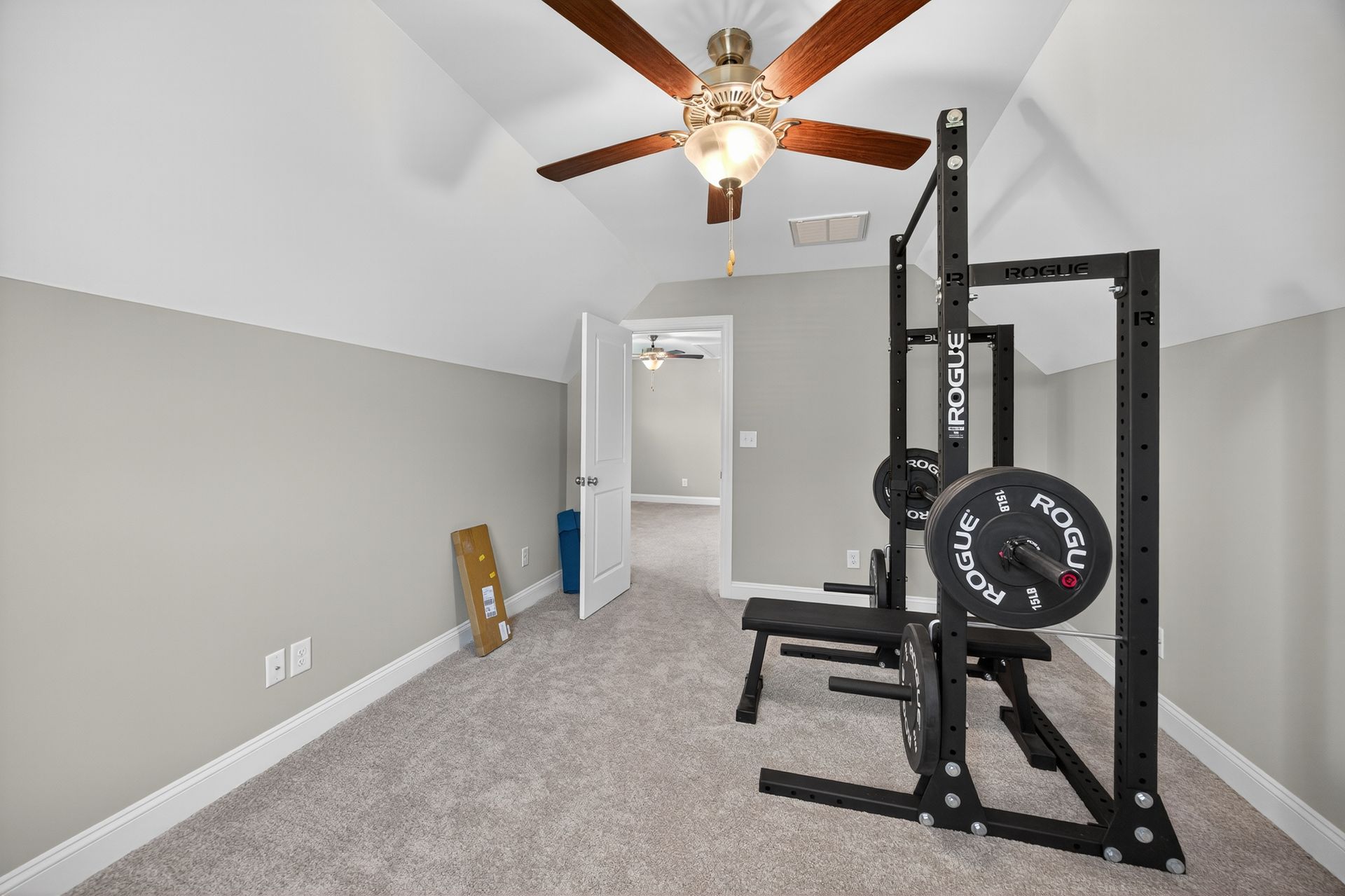 Home exercise room with gray carpet, ceiling fan, and black power rack with weight bench.