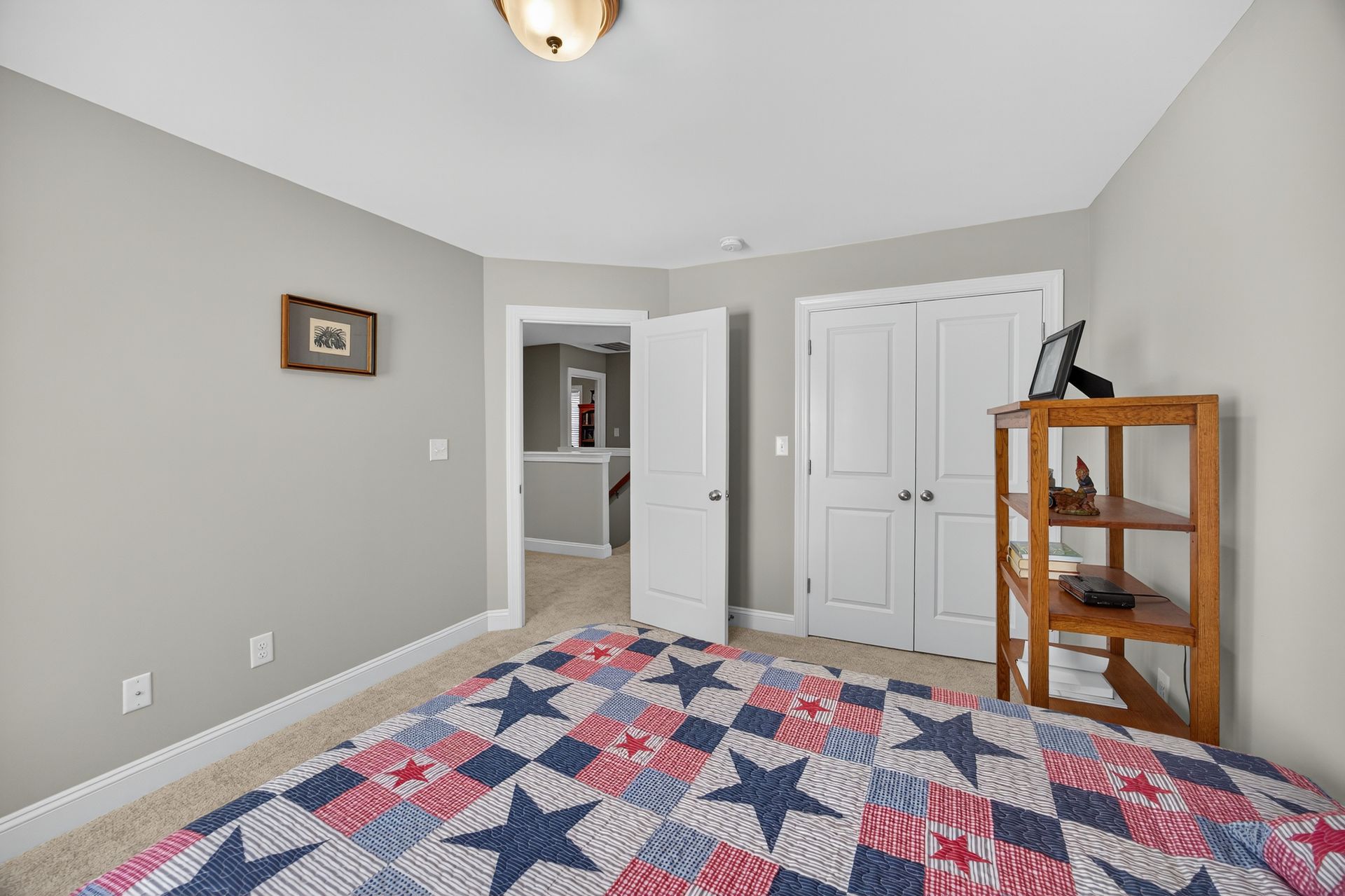 Empty bedroom with gray walls, star-pattern quilted bedspread, and white closet doors.