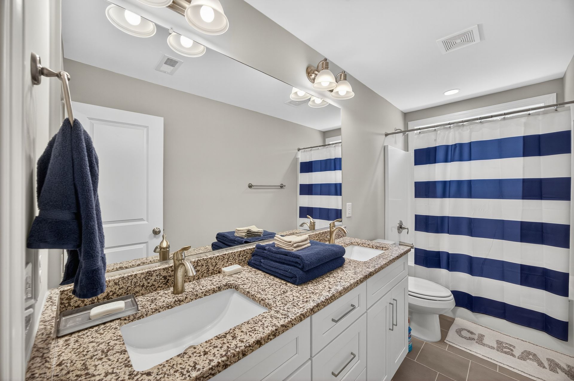 Modern bathroom with granite double vanity, large mirror, and blue-and-white striped shower curtain