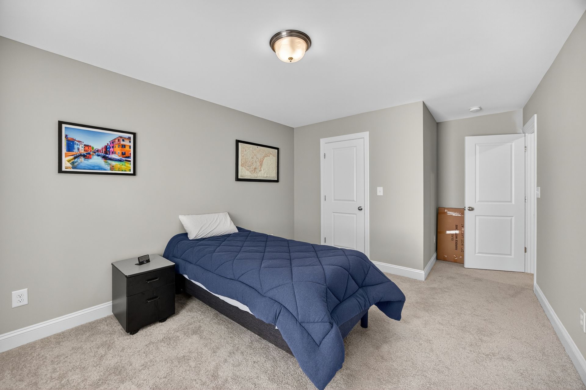 Small bedroom with a blue bedspread, two wall art pieces, carpet, and an open door to a bathroom.