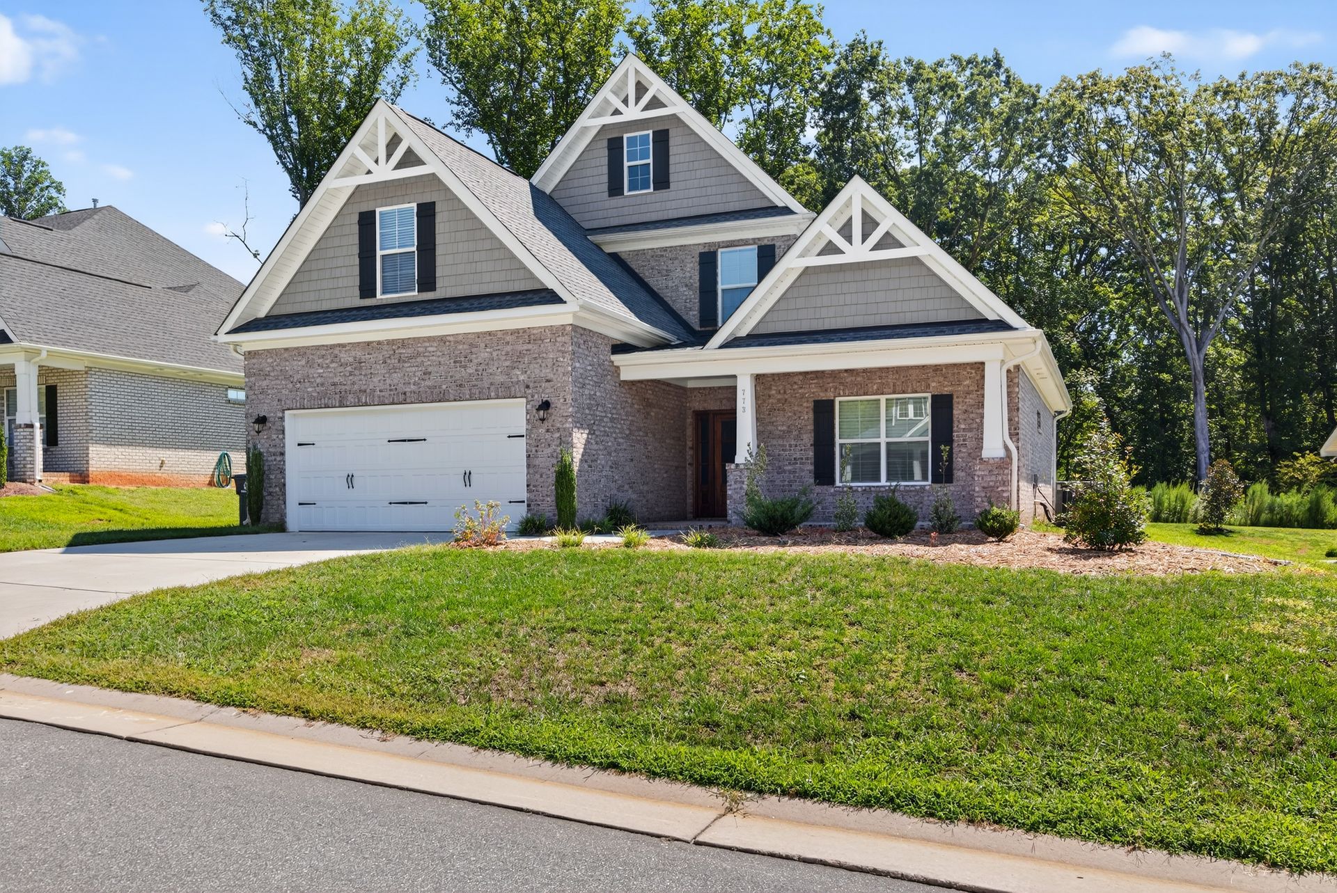 Suburban two-story brick house with white garage, gabled roof, and front lawn on a sunny day