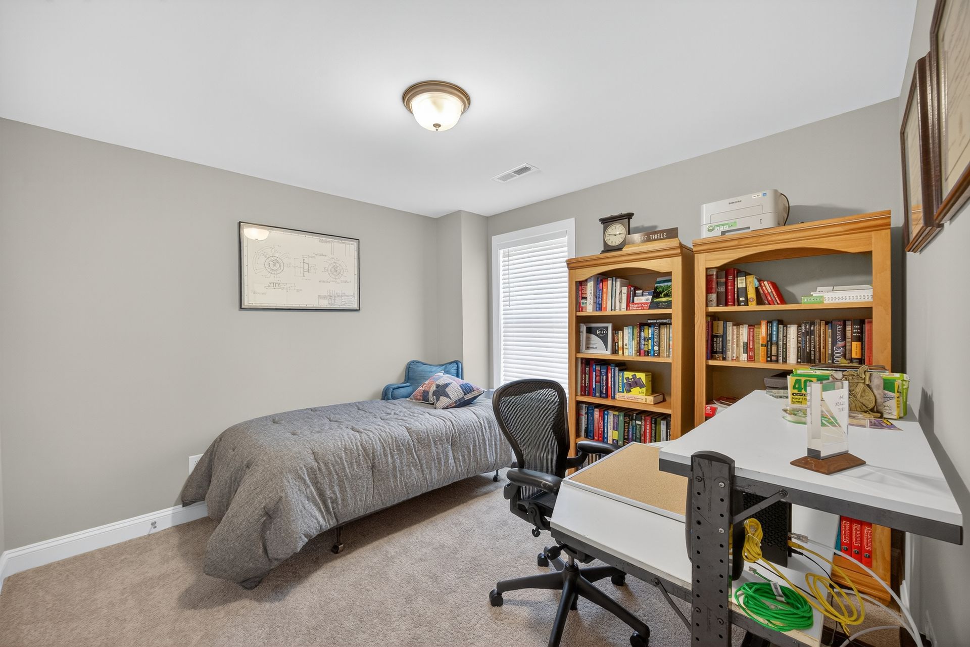 Small bedroom with a bed, desk, chair, and bookshelves in gray and white tones