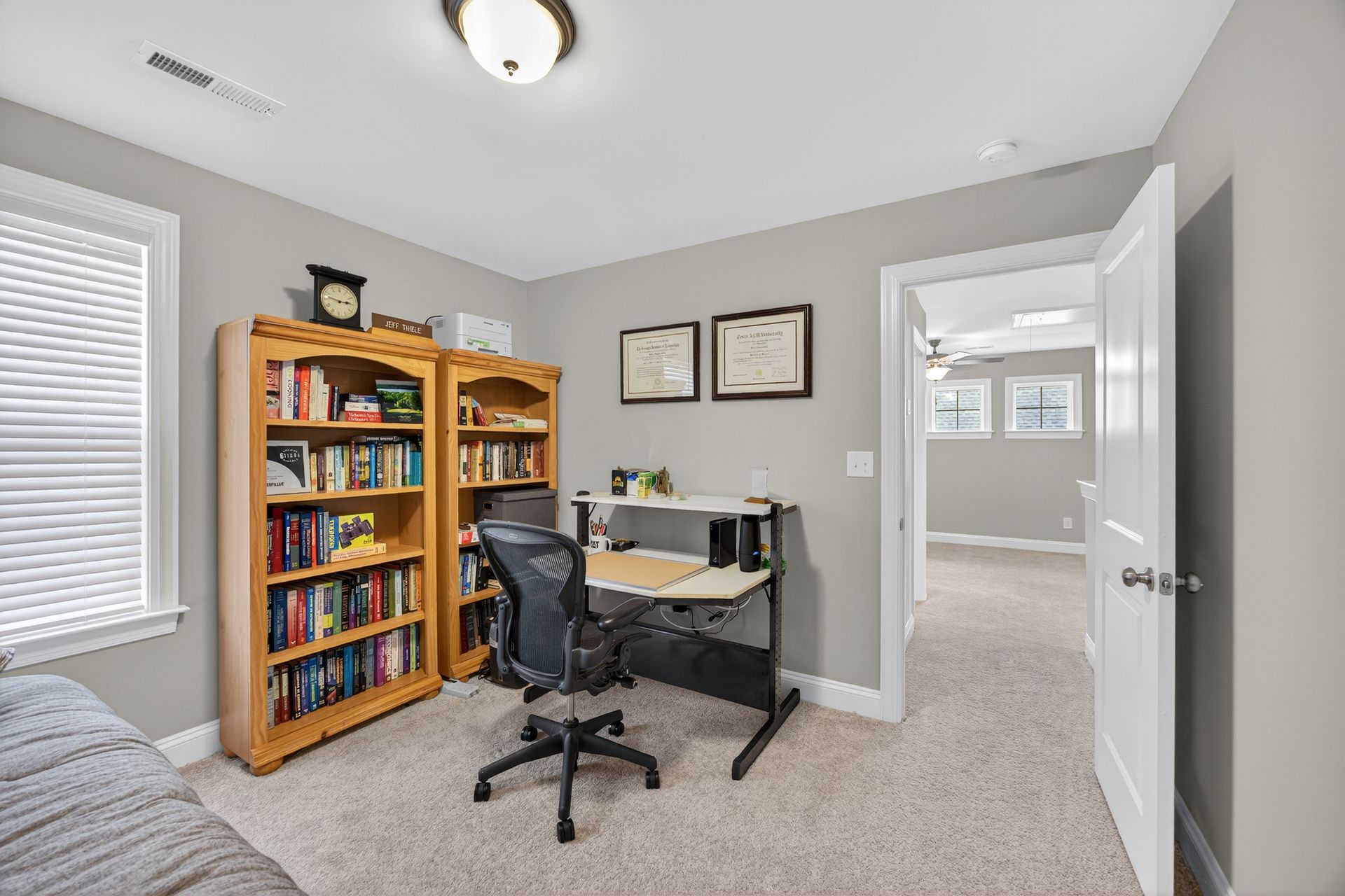 Home office with desk, bookshelf, computer chair, and beige carpet in a gray room
