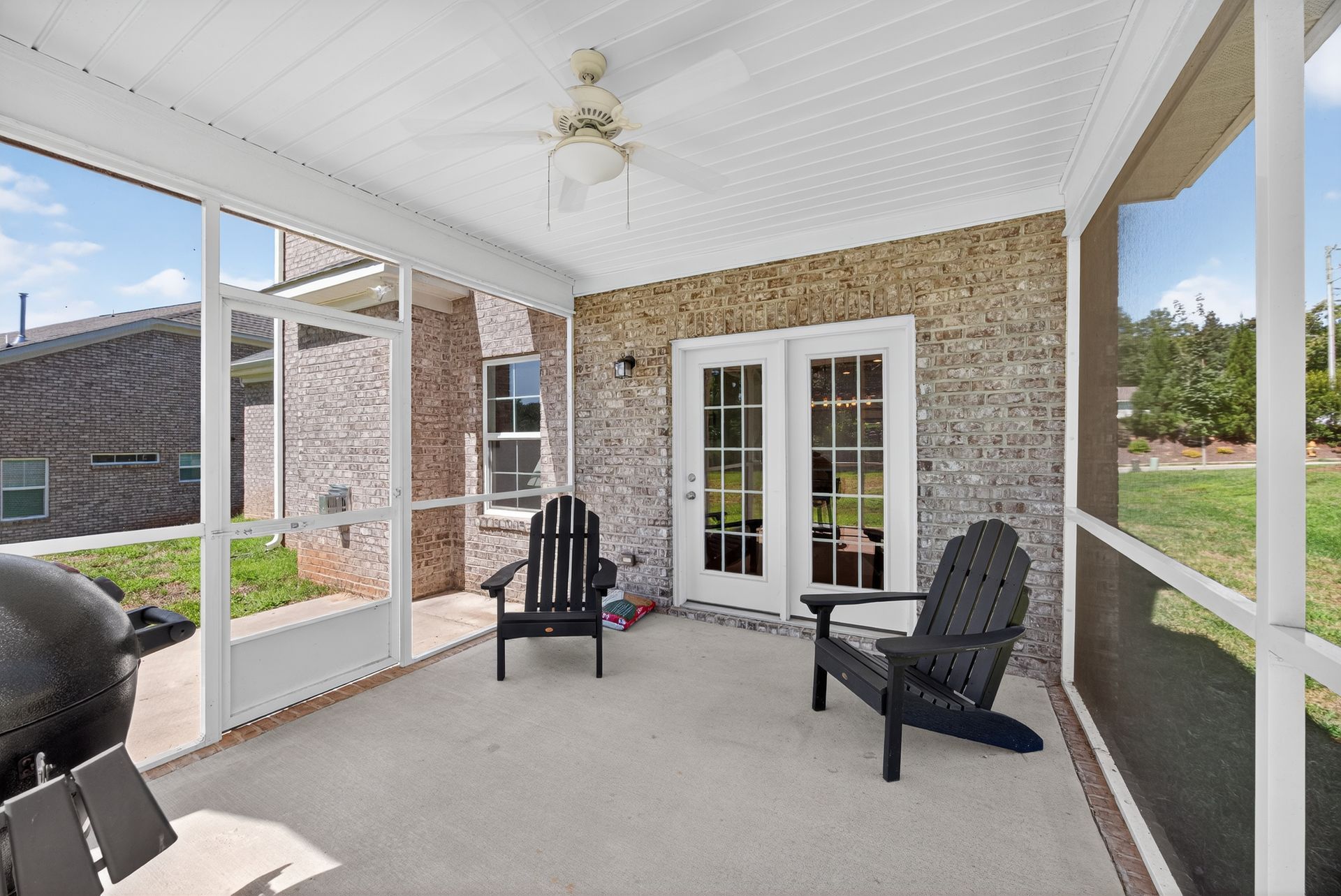 Screened porch with white ceiling, black chairs, and brick exterior wall with French doors