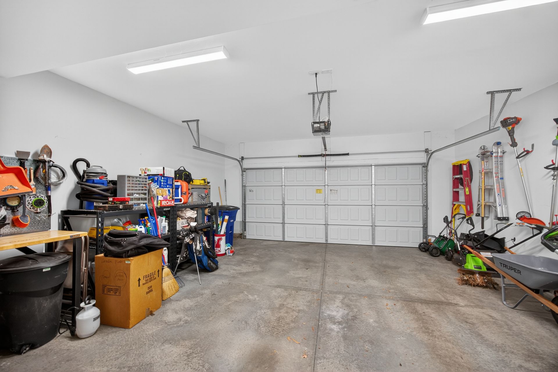 Cluttered garage interior with tools, storage shelves, and a closed white garage door