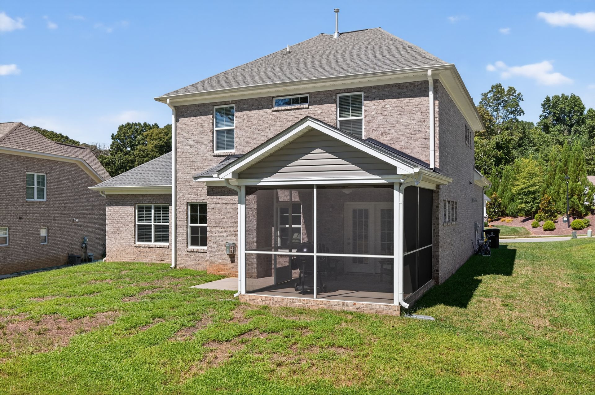 Two-story brick house with screened porch and grassy yard under a clear sky