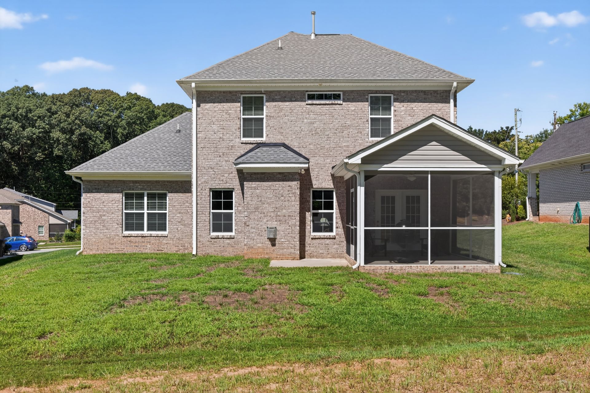 Brick two-story house with screened porch and grassy backyard under a clear sky
