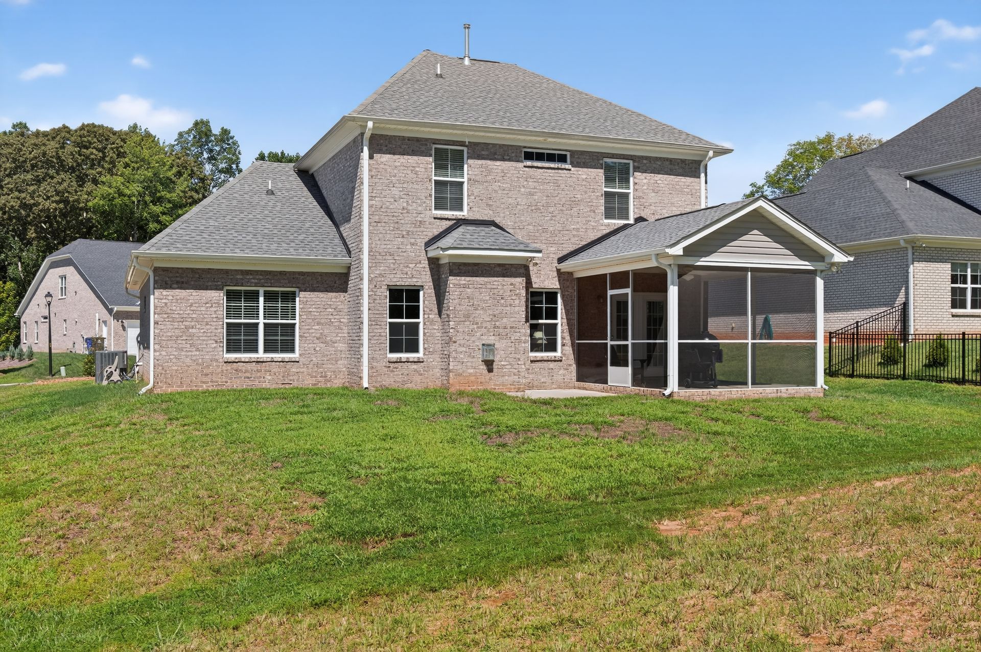 Two-story brick house with screened patio and large grassy backyard under a blue sky