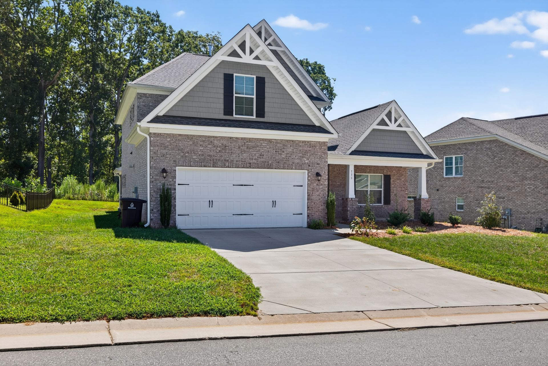 Suburban house with white garage, gray roof, front lawn, and driveway under a clear sky