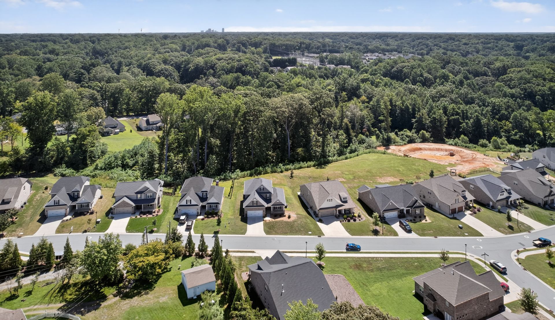Aerial view of a suburban neighborhood with houses, trees, roads, and a baseball field at the edge of a forest