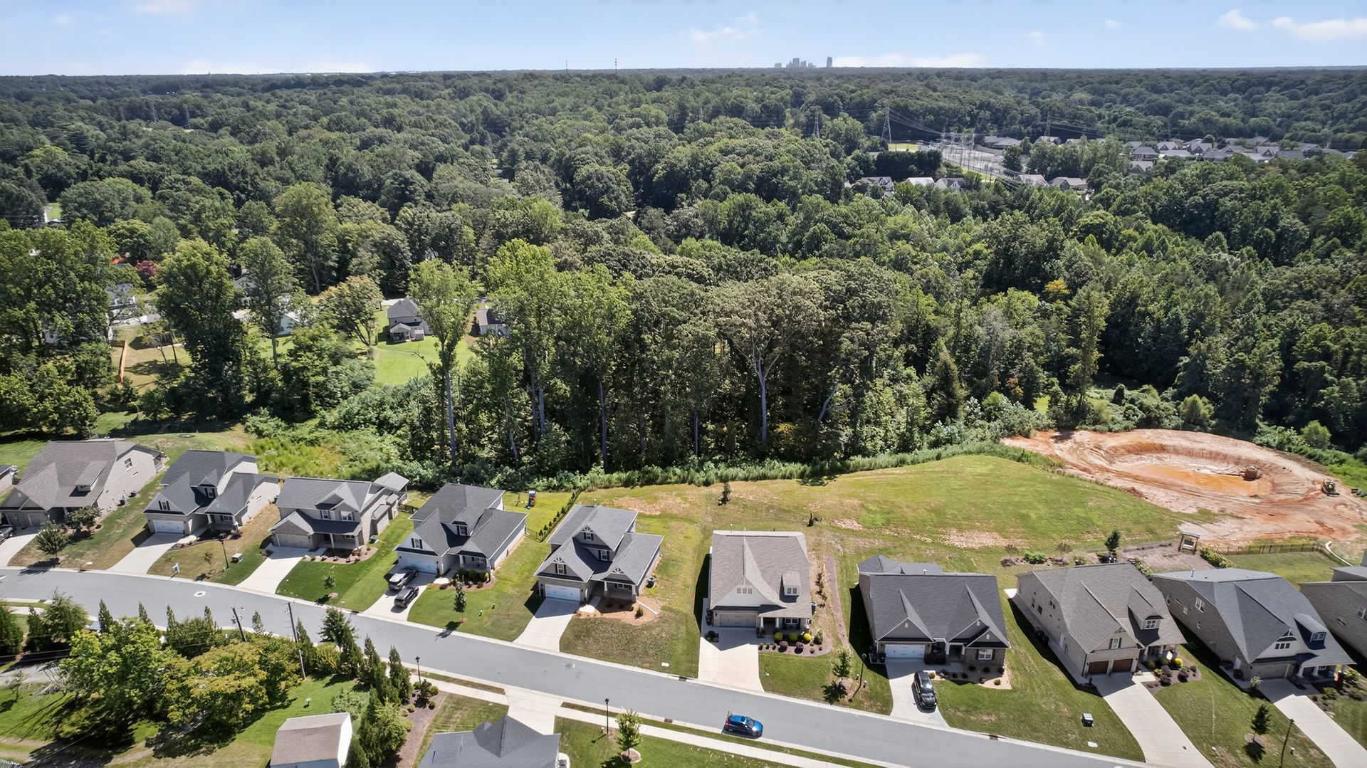 Aerial view of suburban houses bordering a wooded area and a cleared construction lot