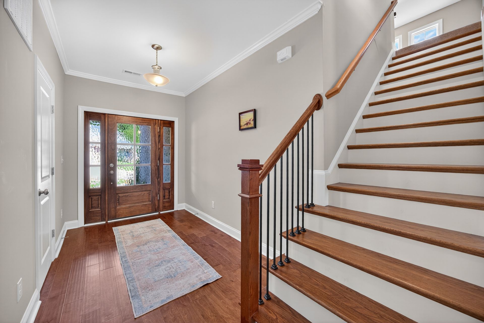 Bright entryway with staircase, hardwood floors, rug, and glass front doors