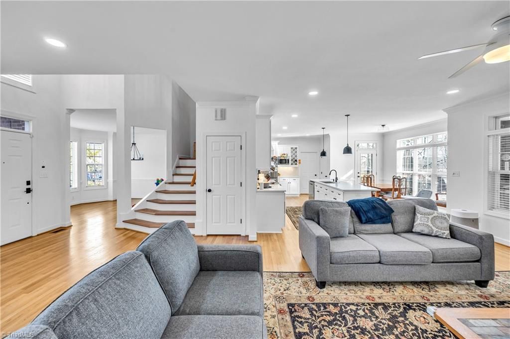 Bright open living room with gray sofas, white stairs, hardwood floors, and large windows