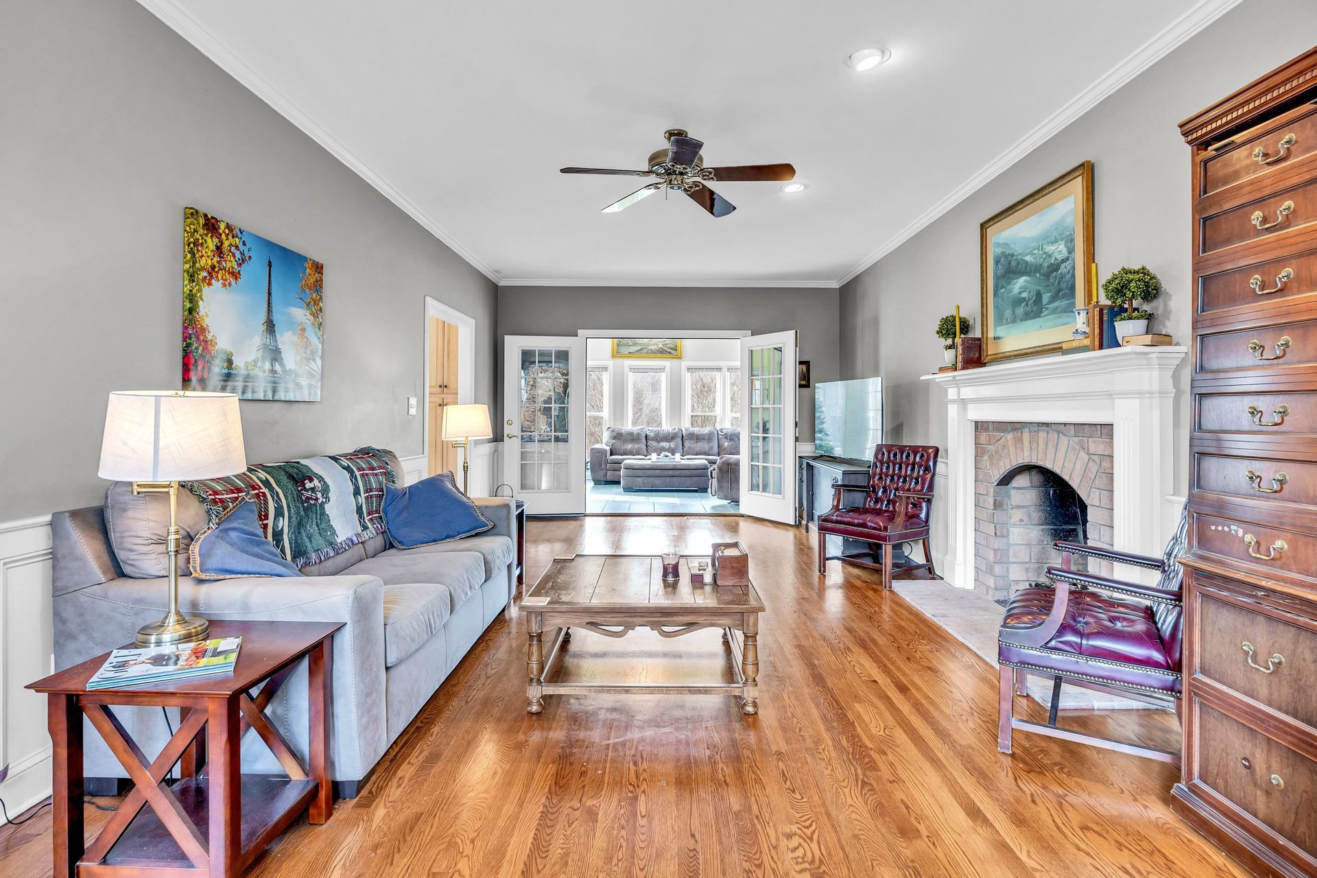 Bright living room with gray sofa, hardwood floors, fireplace, and French doors to a patio.