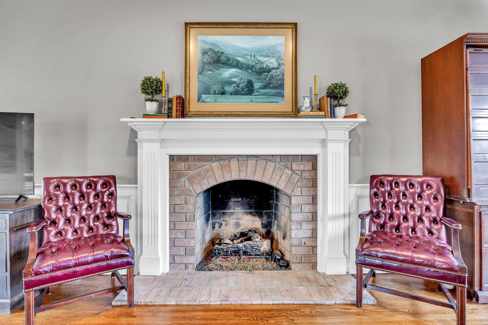 Living room with a white mantel fireplace, framed seascape, and two burgundy chairs